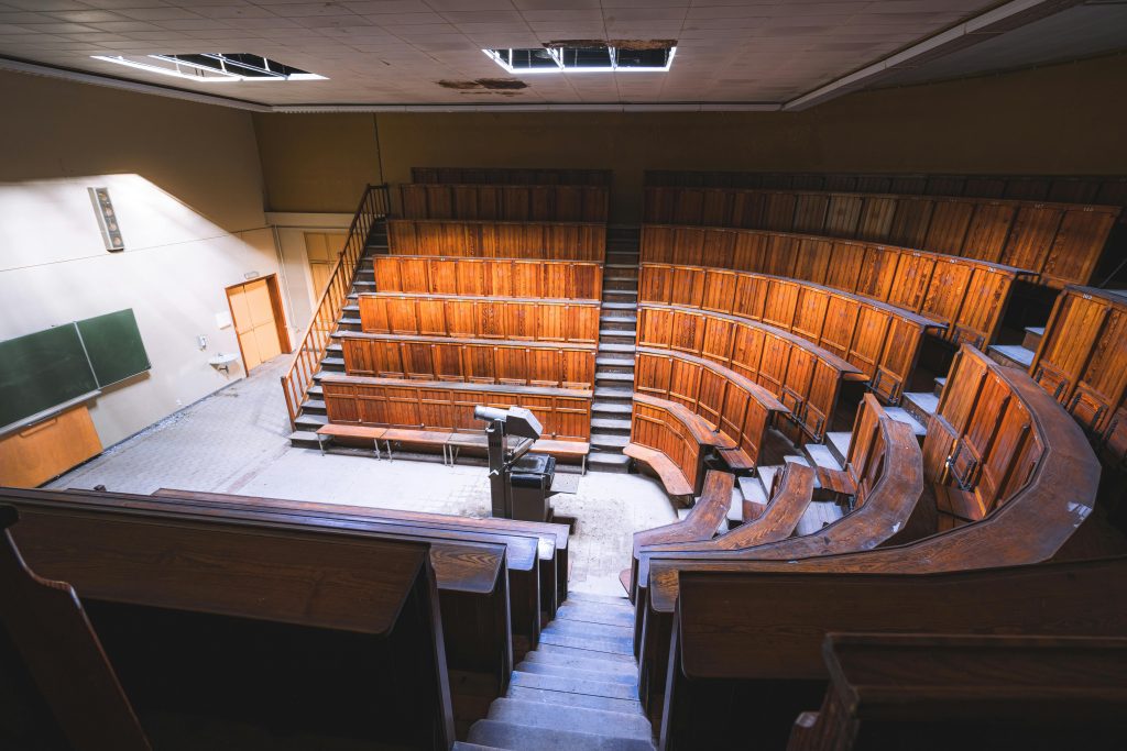 Empty vintage lecture hall with wooden seats and chalkboard, evoking academic nostalgia.