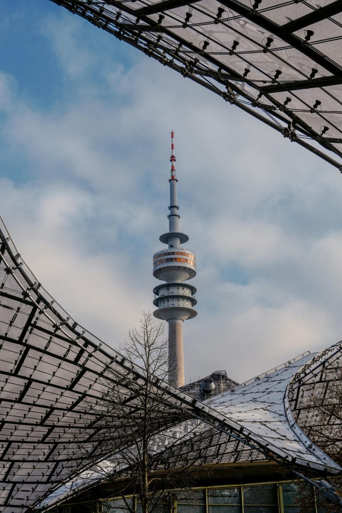 Olympiaturm under a blue sky, framed by Munich Olympic Park's unique architecture.