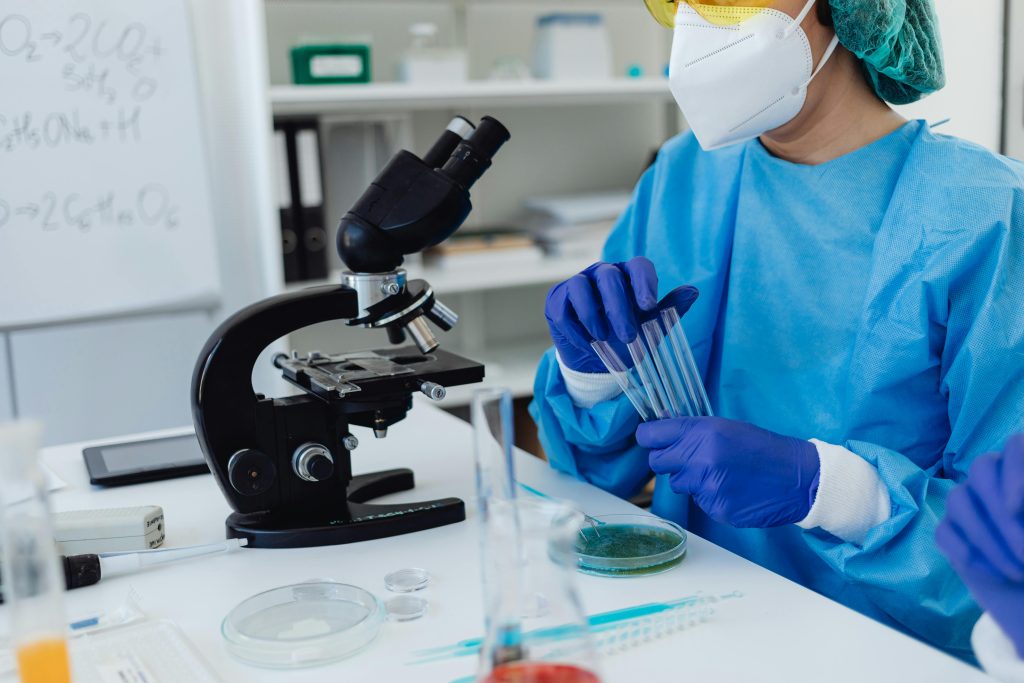 Researcher in PPE using microscope and analyzing samples in a laboratory setting.